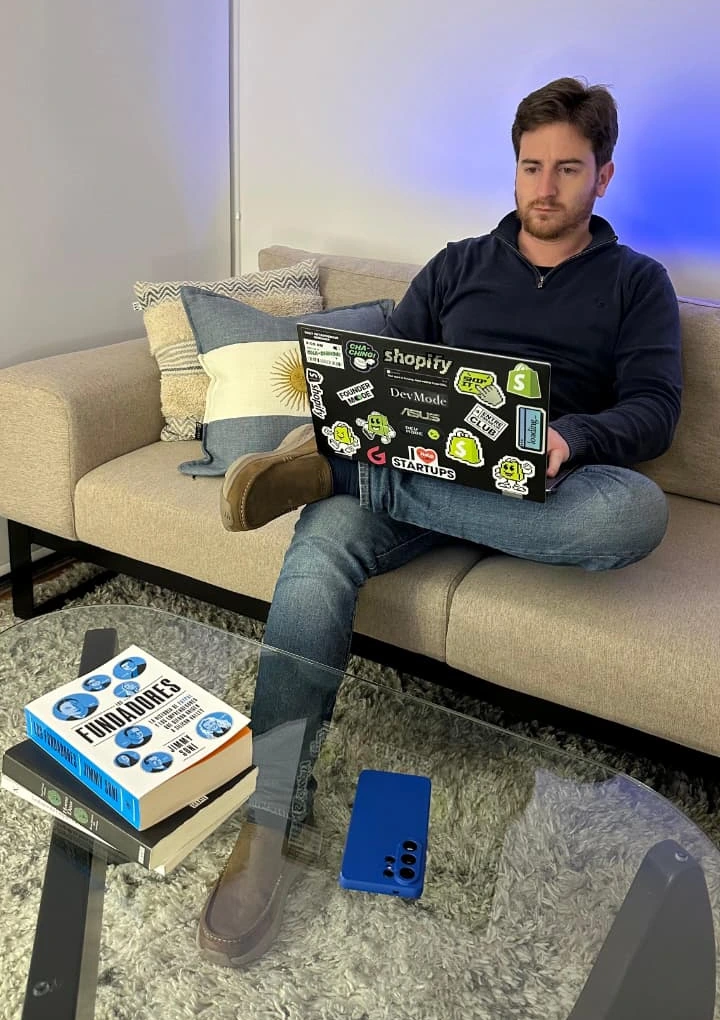 Max Abella en un sillón, trabajando en una laptop llena de stickers de Shopify